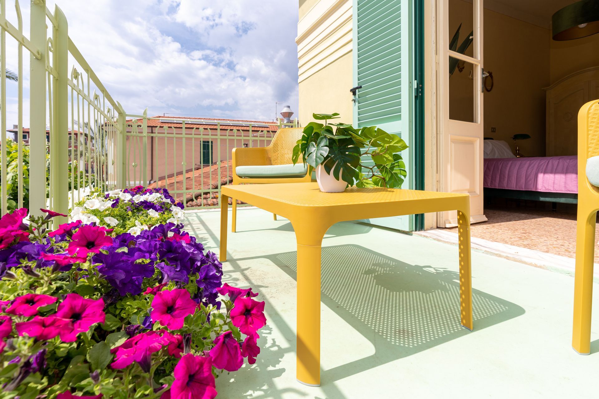 Balcony with yellow table and chairs, overlooking a cityscape, with colorful flowers.