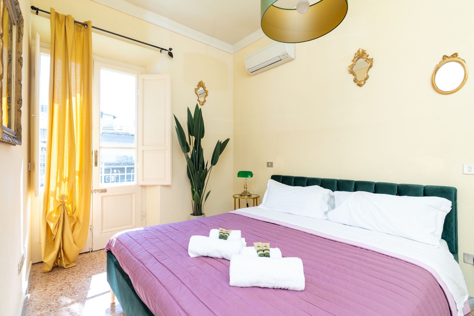 Bedroom with bed, yellow curtains, decorative mirrors, and a plant.