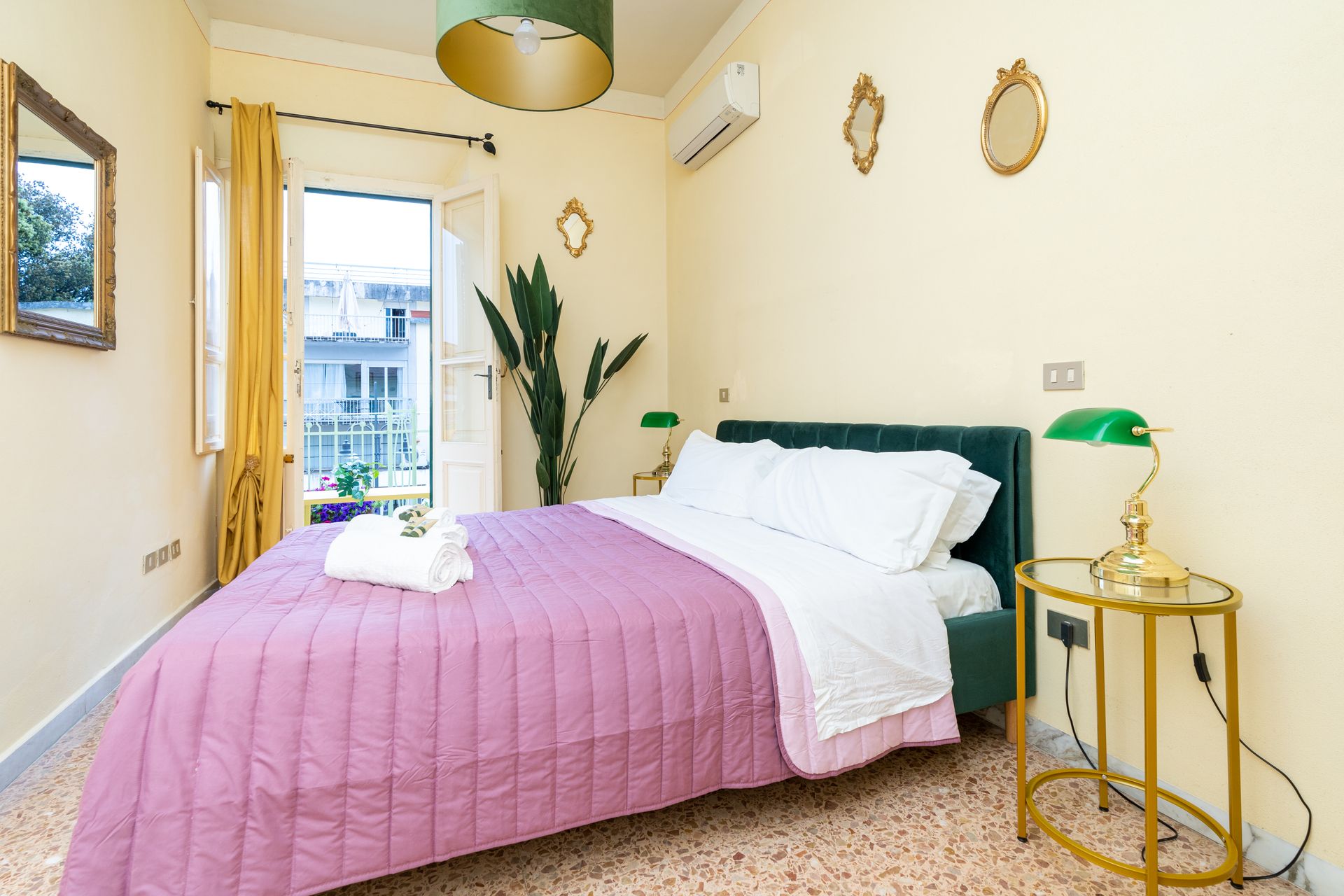 Bedroom with bed, side table, mirror, open balcony door, and decorative gold accents.