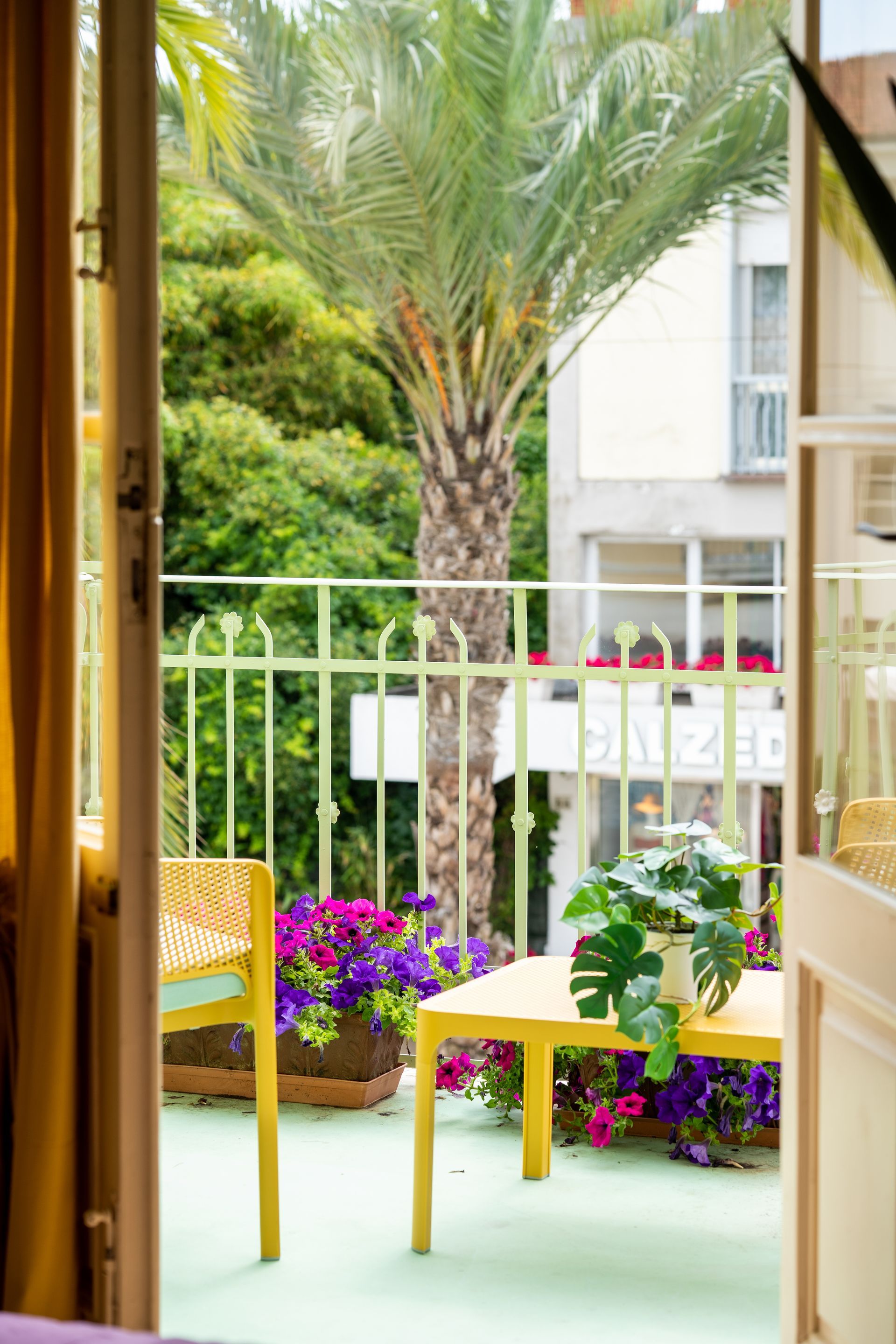 Yellow balcony with table, chair, flowers, and palm tree view.