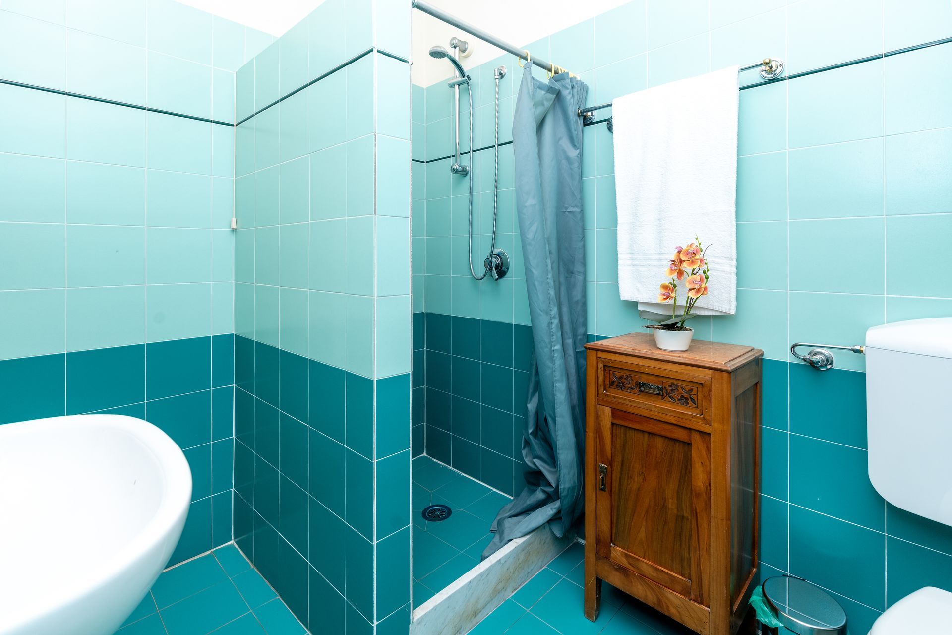 Bathroom with turquoise tiles, a shower, wooden cabinet, and a white towel.