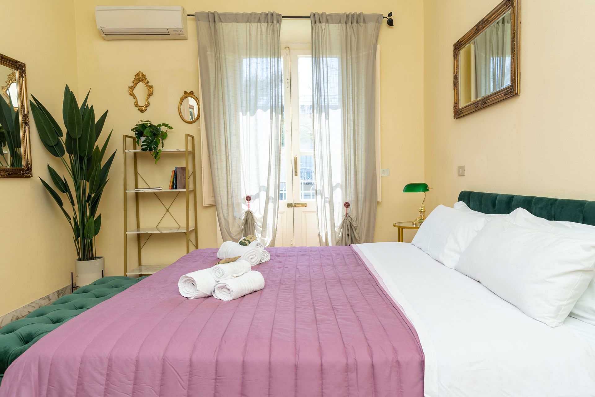 Bedroom with a purple bedspread, sheer curtains, and a plant.