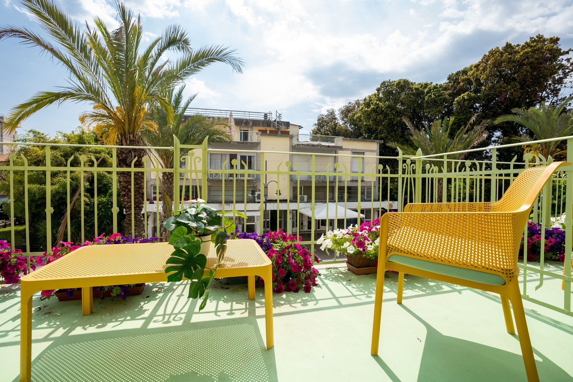 Yellow patio furniture on a balcony with flowers, palm trees, and buildings in the background.