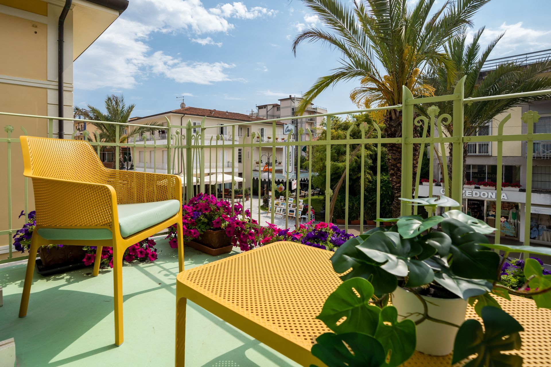 Balcony with yellow furniture, flowers, and view of buildings under a sunny sky.