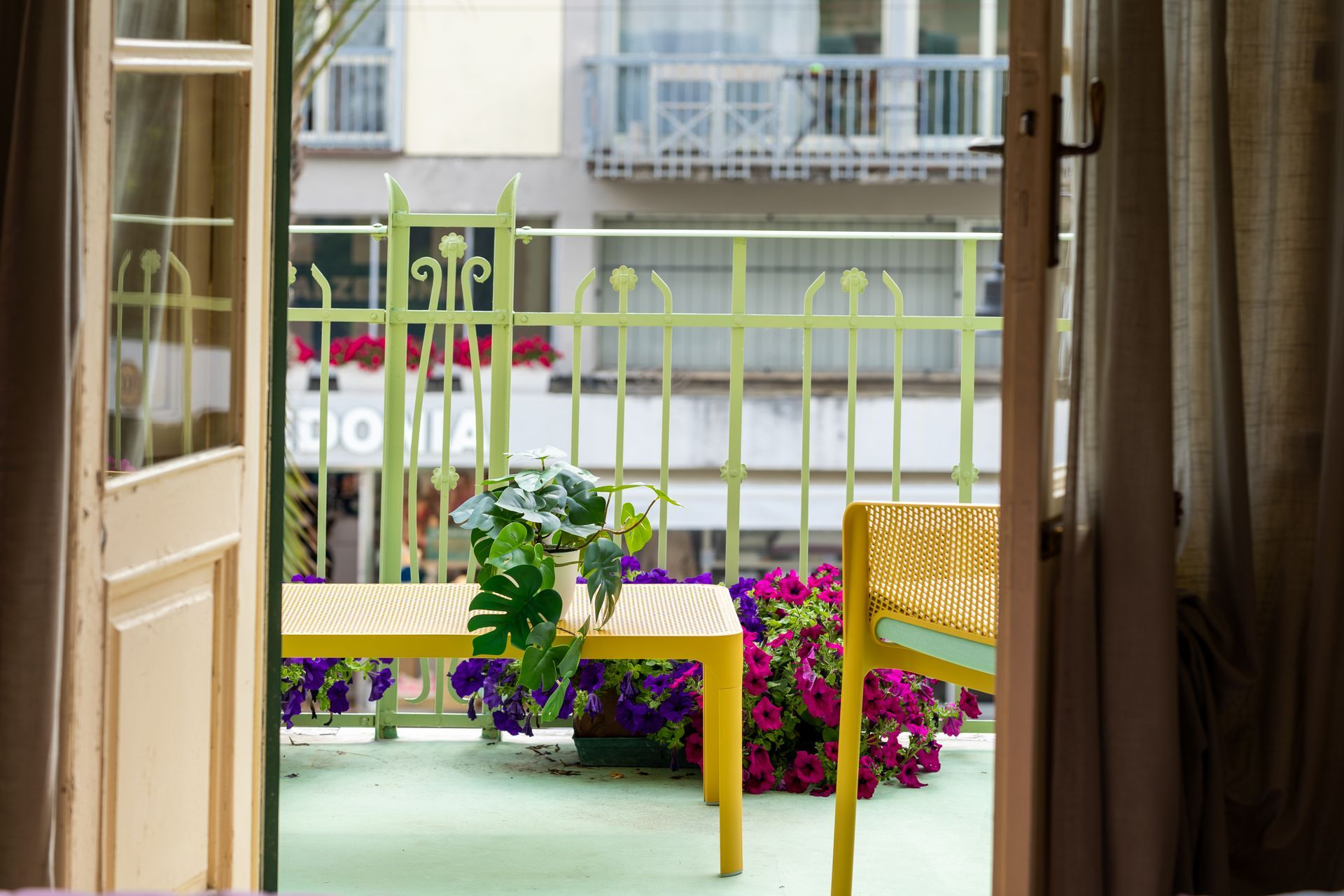 Balcony with yellow furniture, green railing, and flowers, viewed from an open doorway.