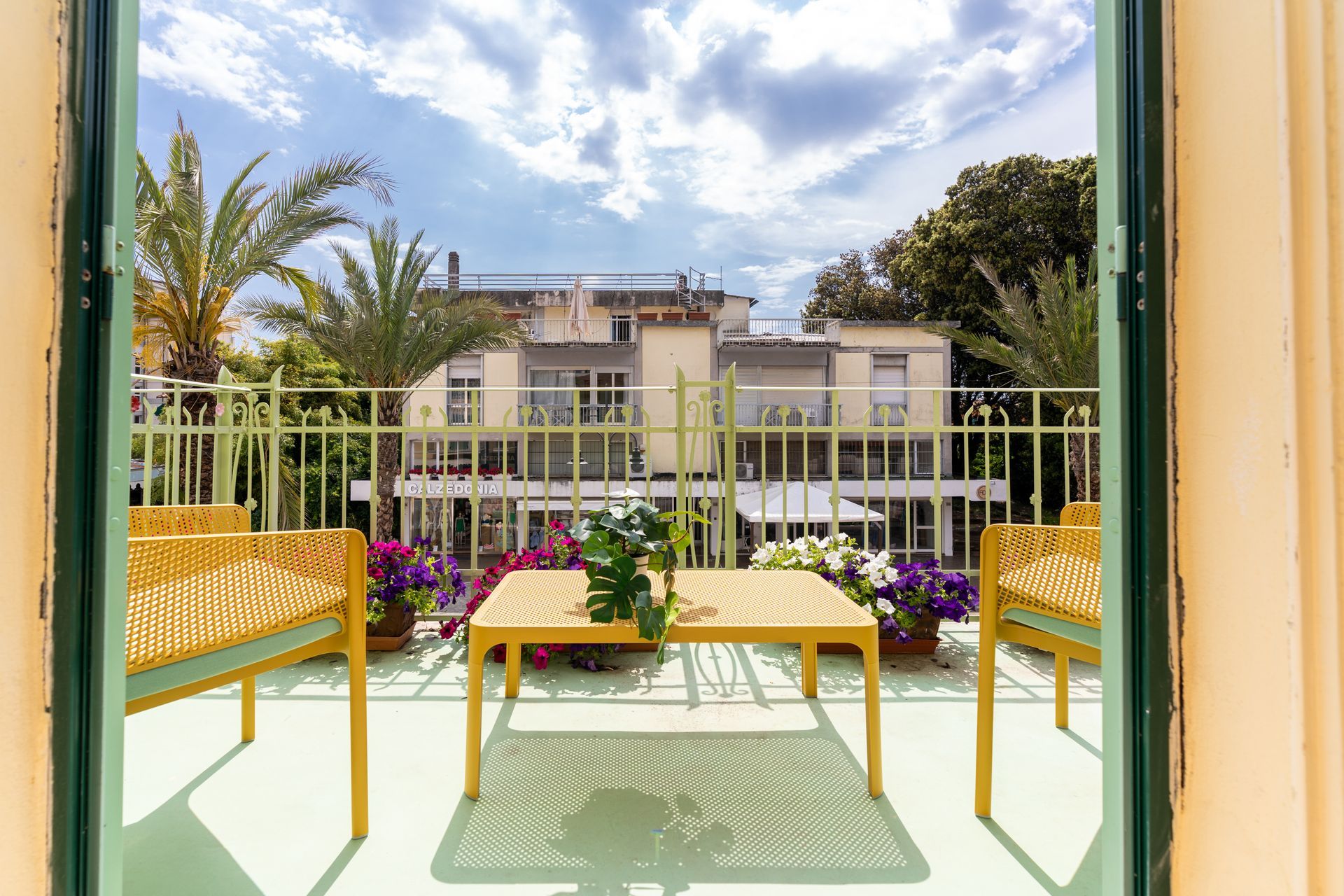 Balcony with yellow furniture, potted flowers, and view of building and sky.