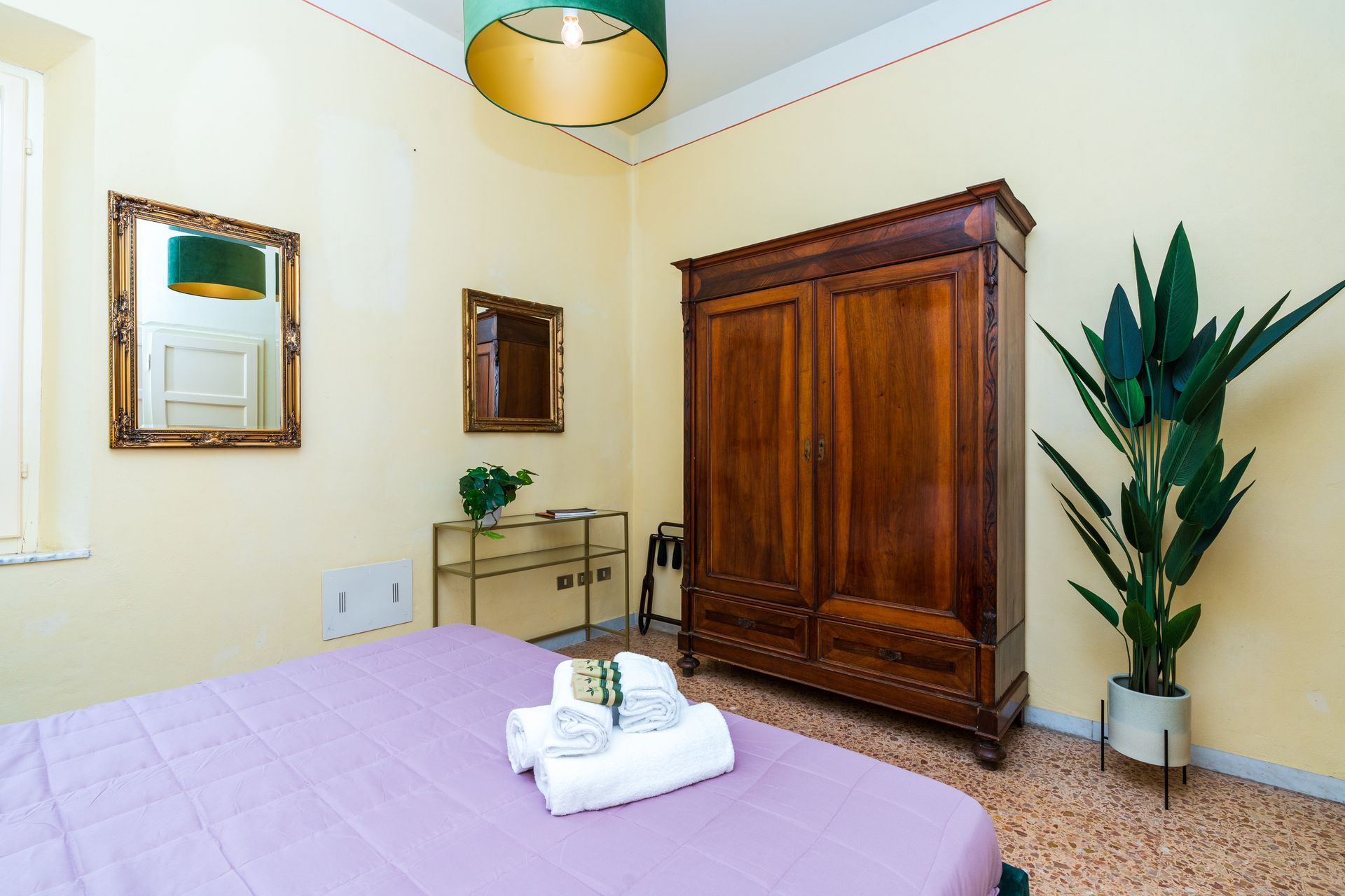 Bedroom with a wooden wardrobe, two mirrors, a bed, and a potted plant. The walls are light yellow.