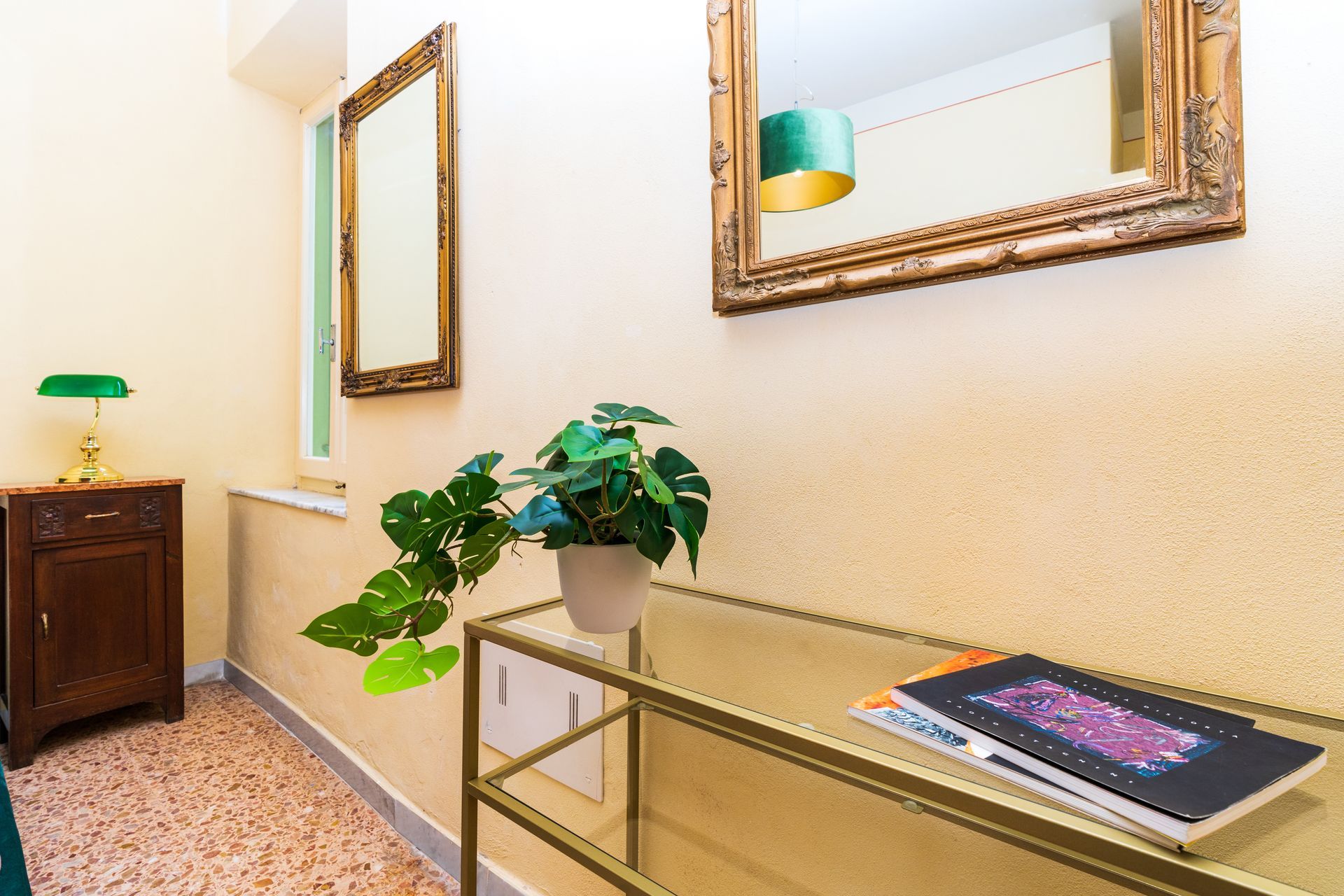 Hallway with mirrors, a small table, a plant, and a table with a book.
