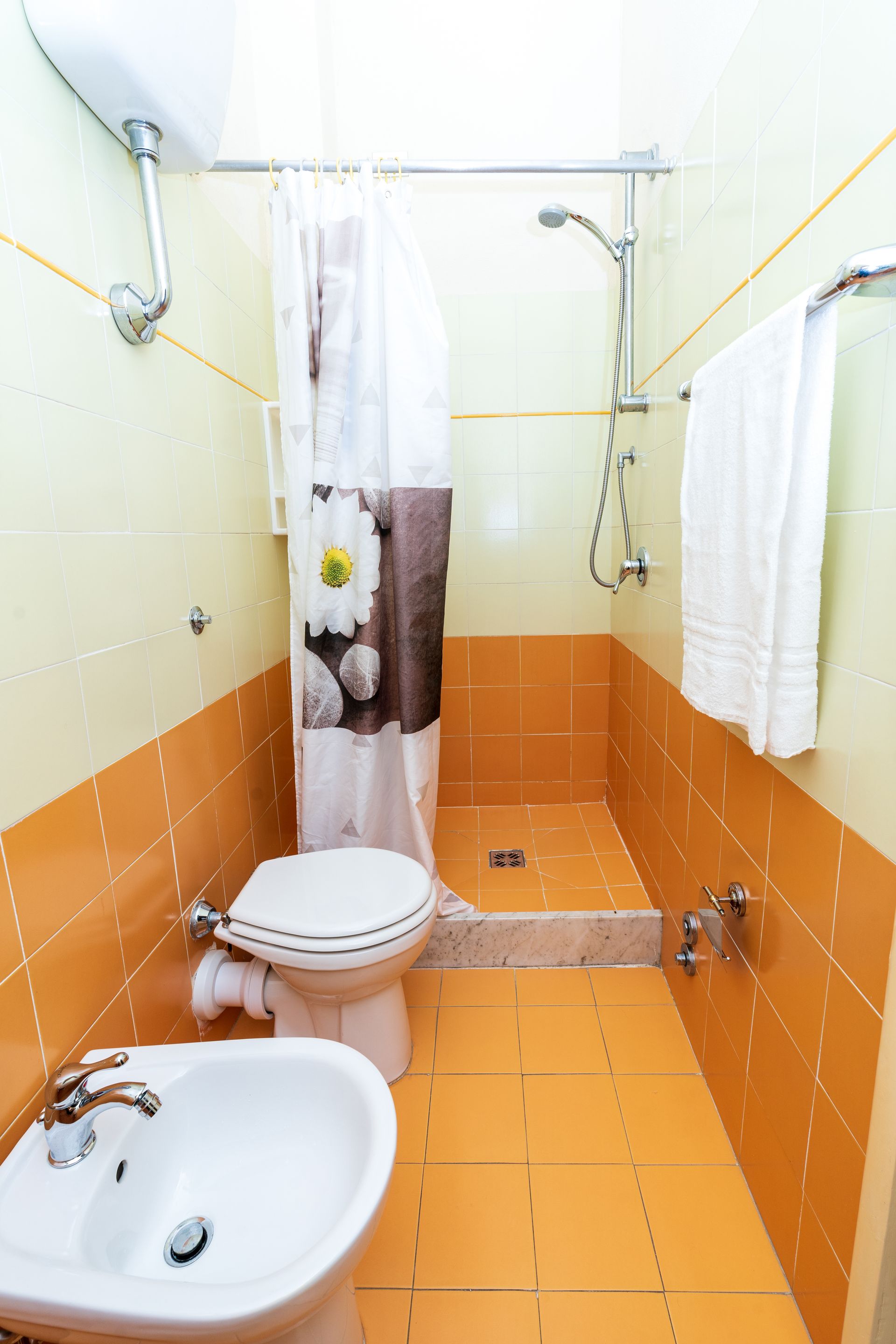 Bathroom with orange tile, toilet, bidet, shower, and white towel.