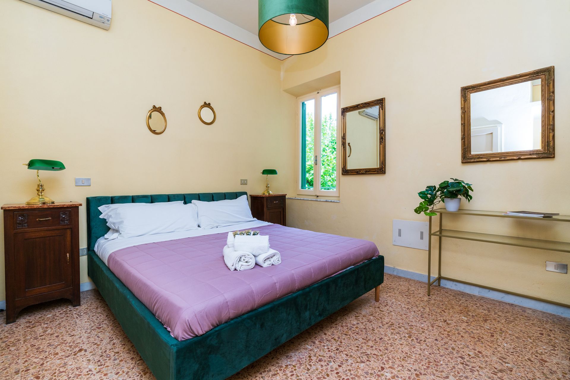 Bedroom with a green bed, lamps, and accents, with a window and mirrors.