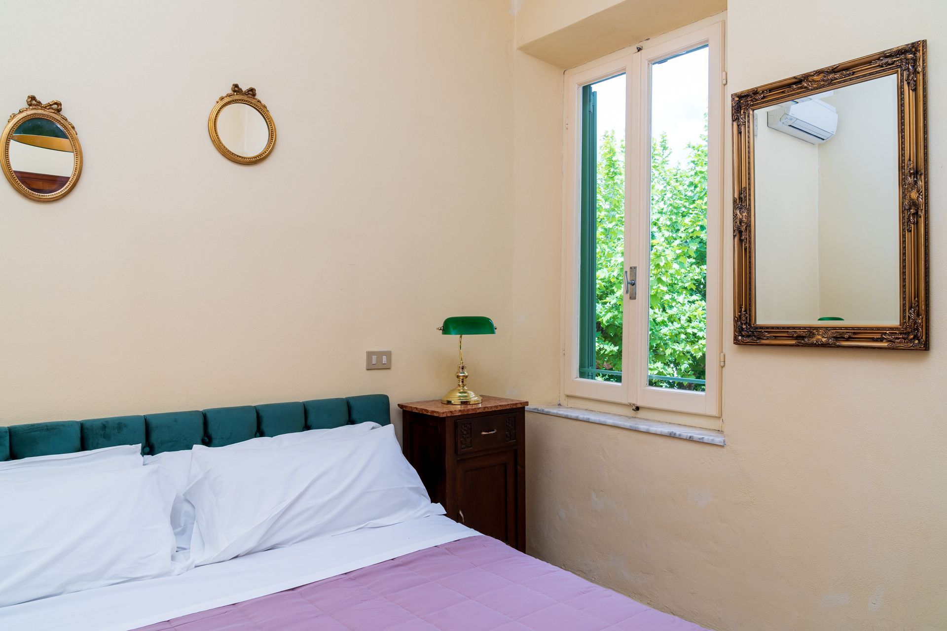 Bedroom with a double bed, nightstand, window, ornate mirror, and wall decor.