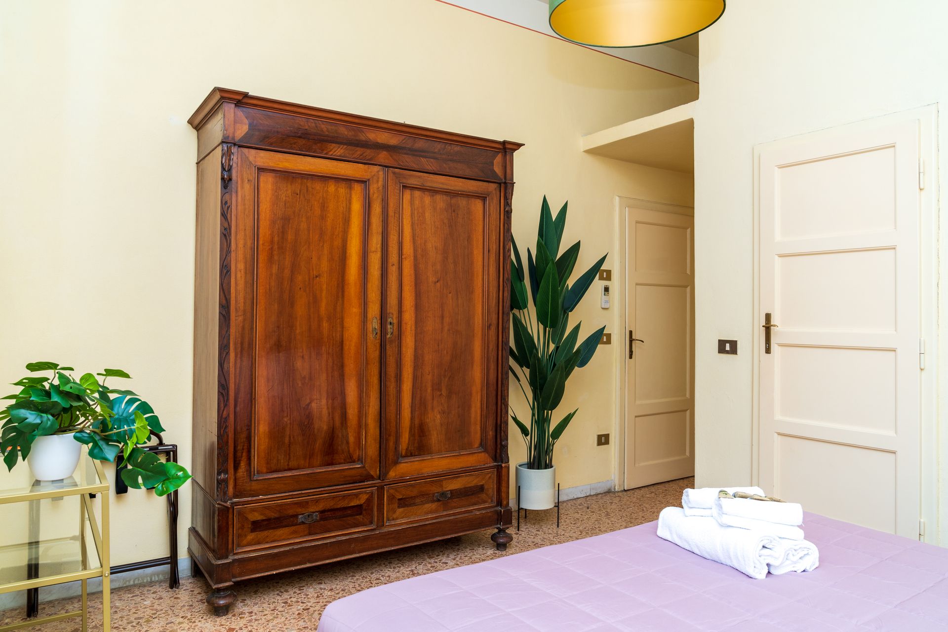 Wooden wardrobe in a bedroom with a plant and white towels on the bed.