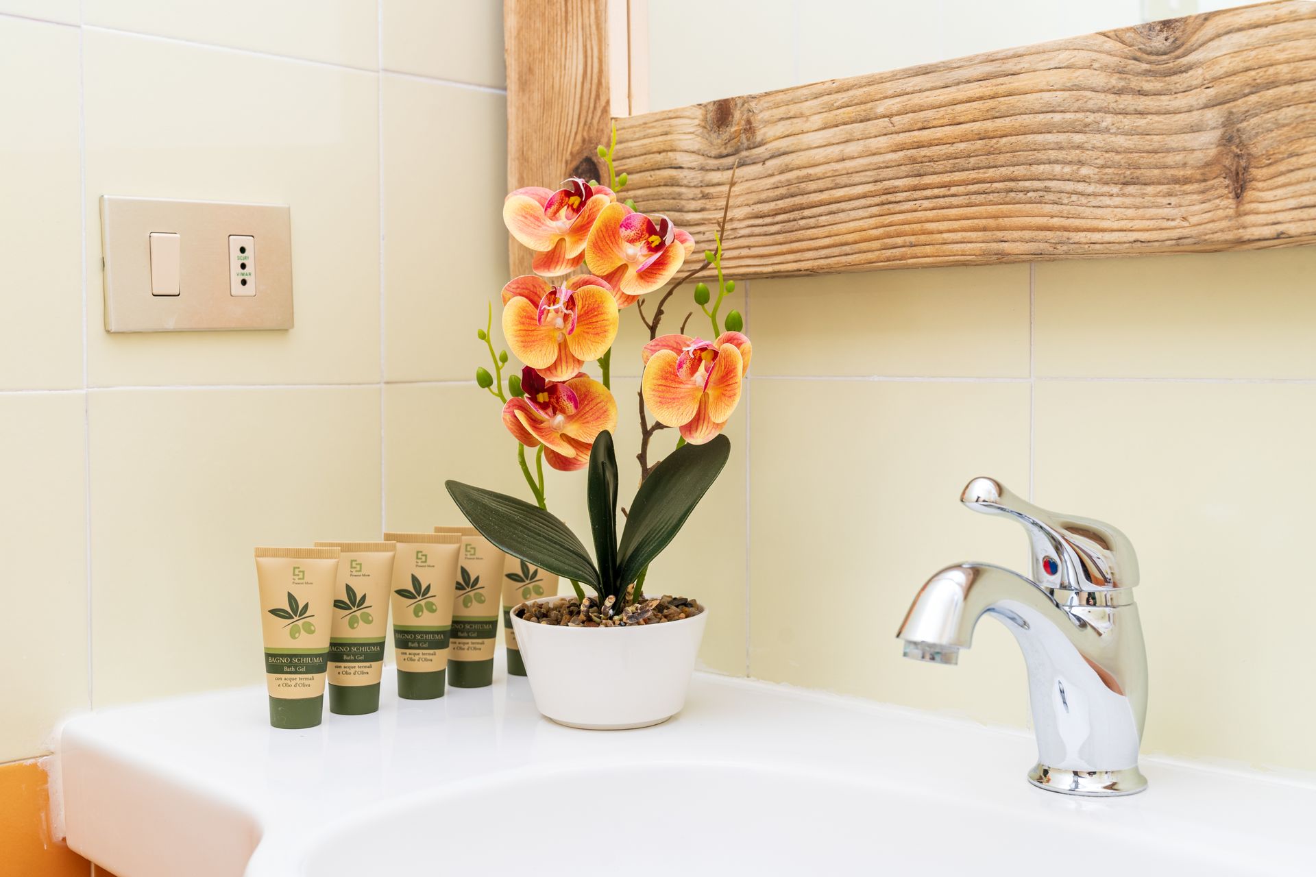 Bathroom sink with orange flower arrangement, toiletries, and faucet. A wooden-framed mirror is above the sink.