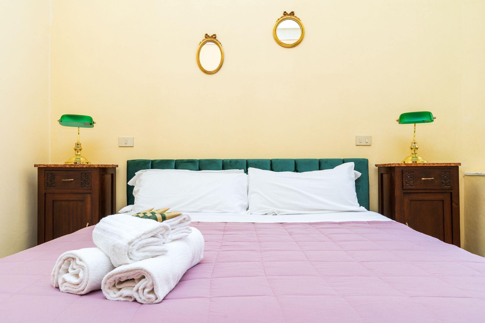 Bedroom with bed, bedside tables, lamps, mirrors, and rolled towels on the bed.