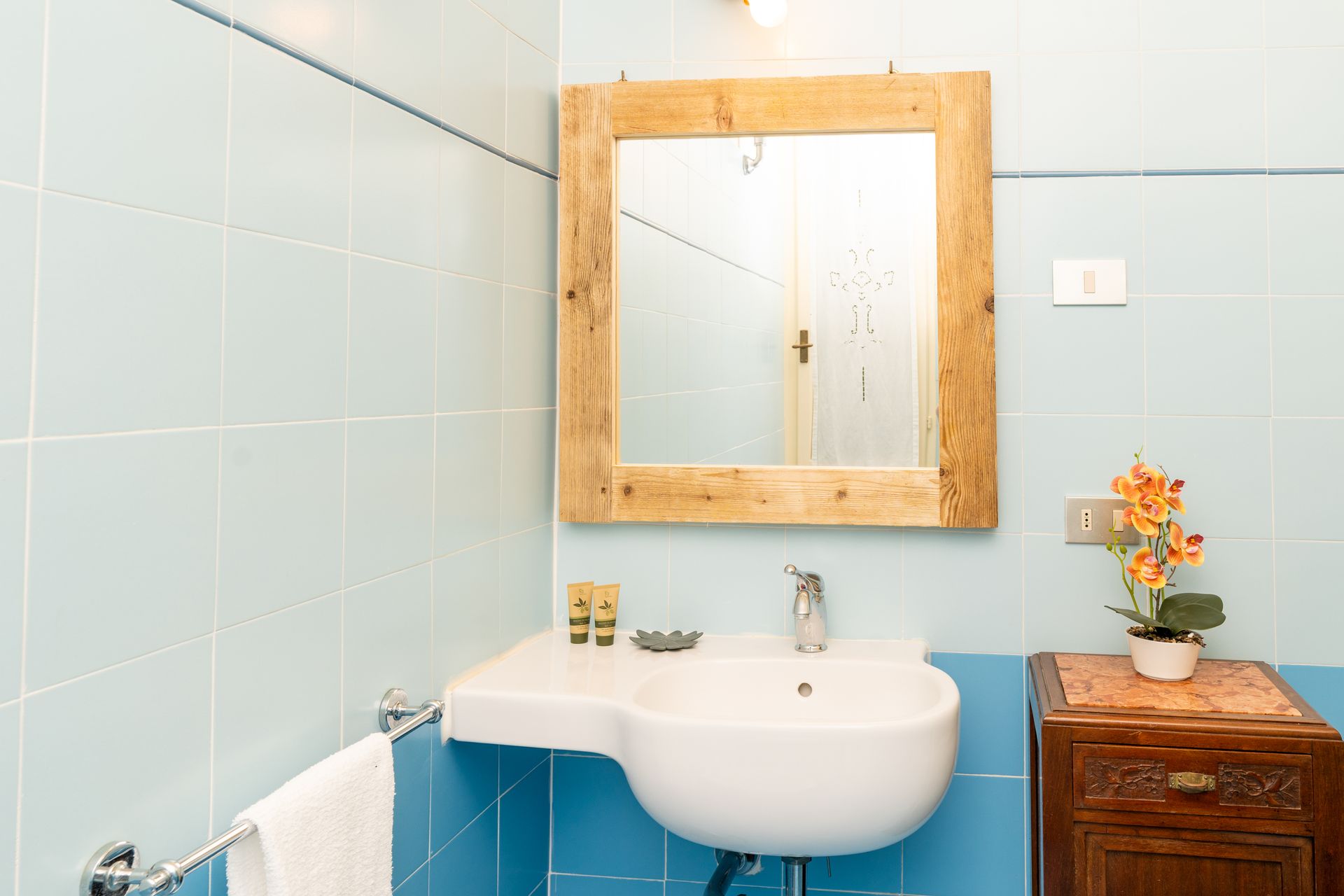 Bathroom with light blue tile walls, a white sink, and a wooden framed mirror.
