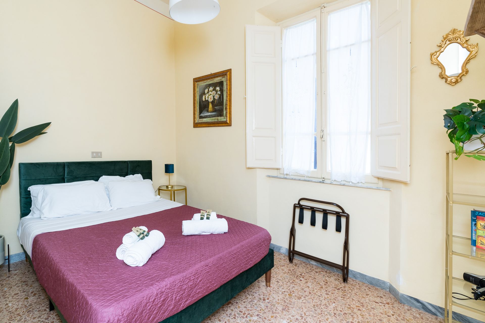 Bedroom with a double bed, open window, and decorative mirror. Pale yellow walls.