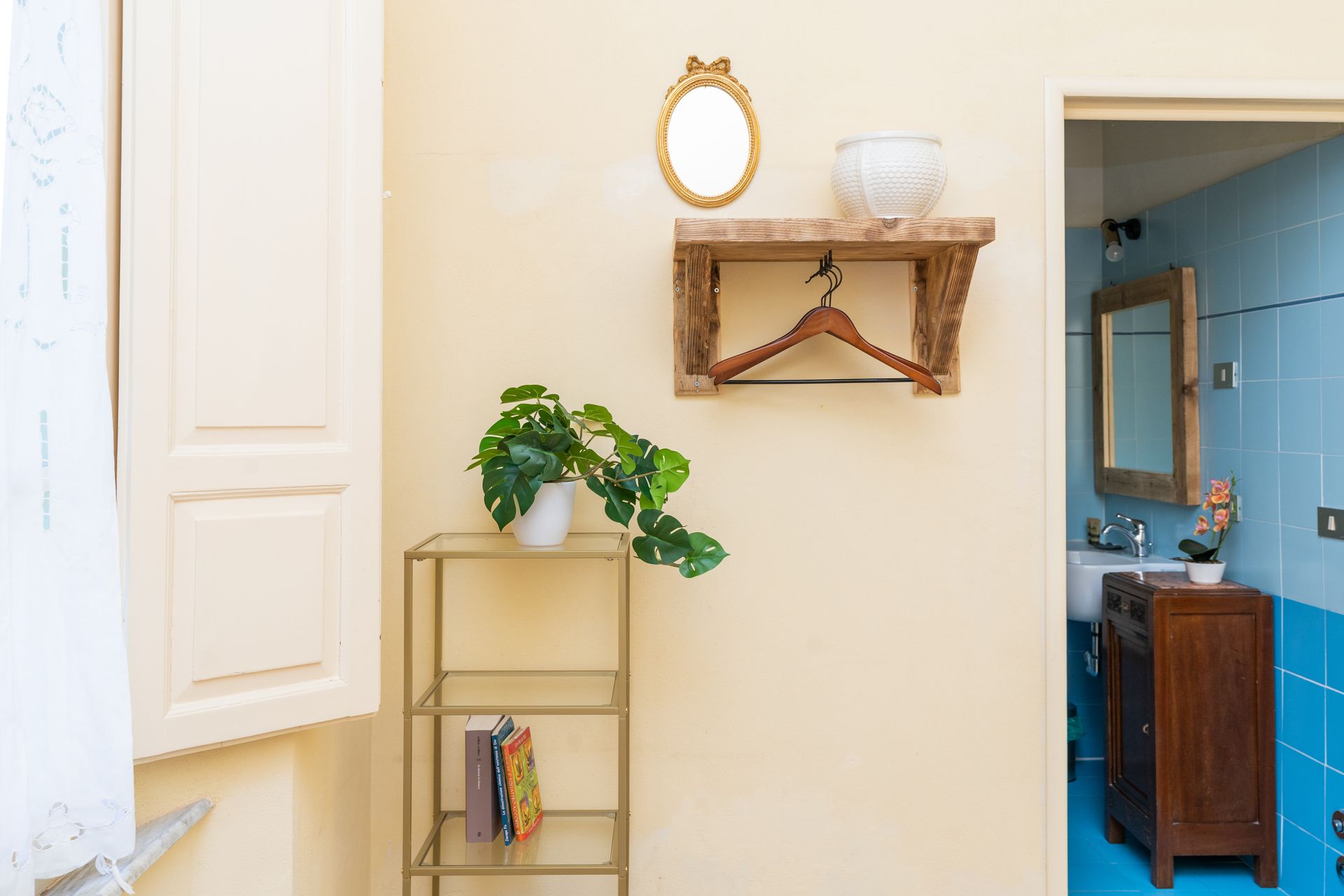 Beige wall with open door to blue bathroom; gold shelf, mirror, and plant.