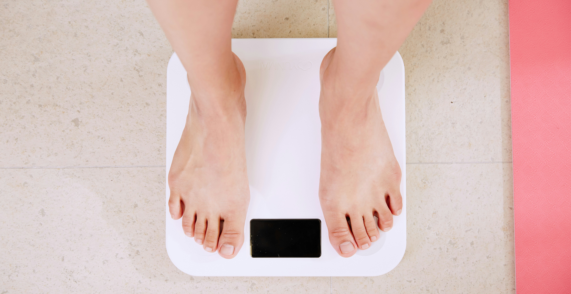 Feet standing on a white digital scale. A pink mat is to the side.