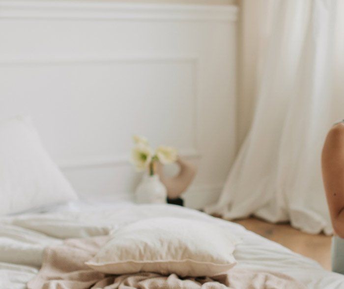 A woman is sitting on a bed with a pillow and a blanket.