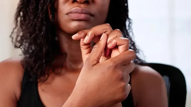 Close-up of a person clasping their hands near their face, with a neutral expression against a blurred background.