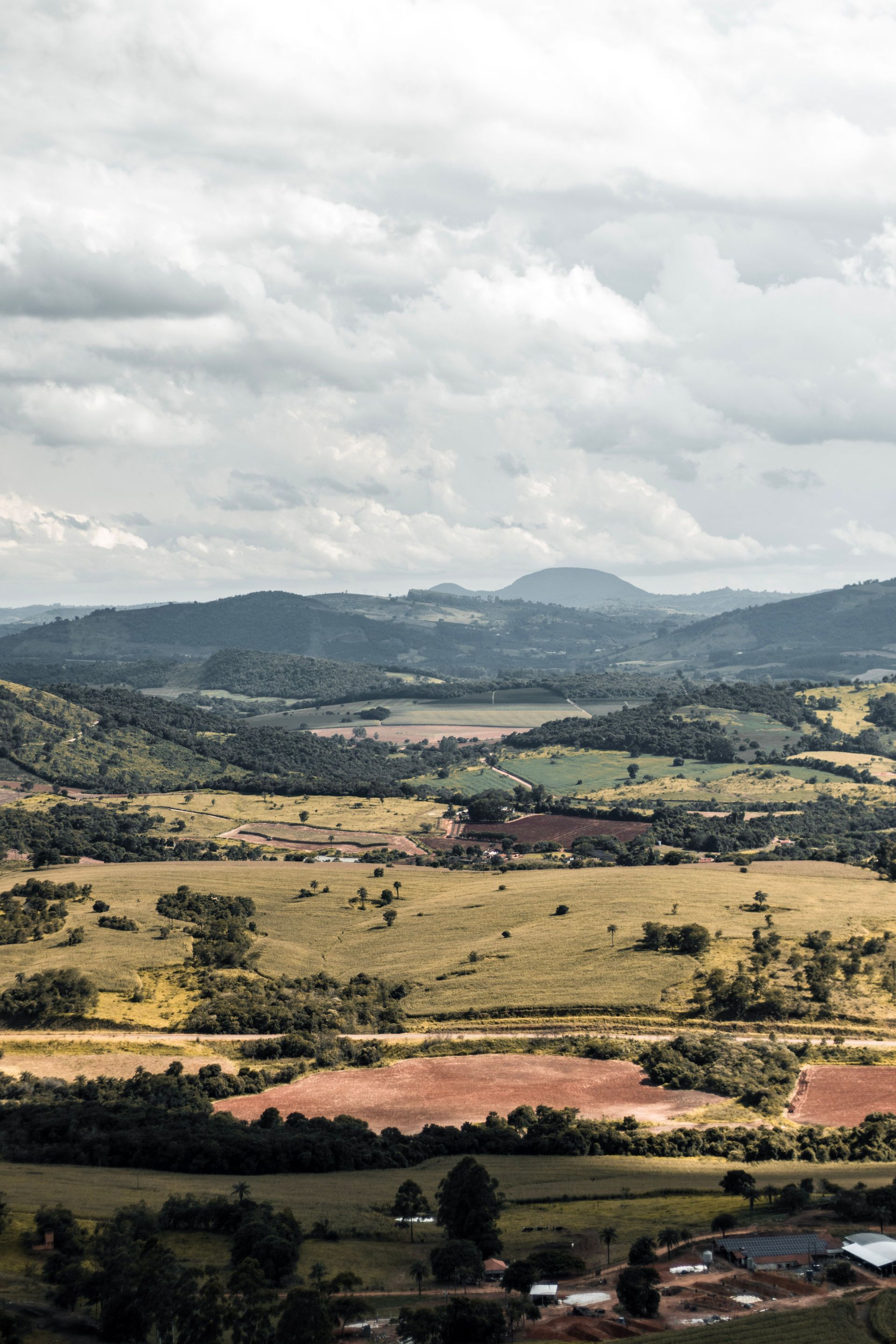 Wide rural valley with patchwork fields, rolling hills, and cloudy sky in the distance