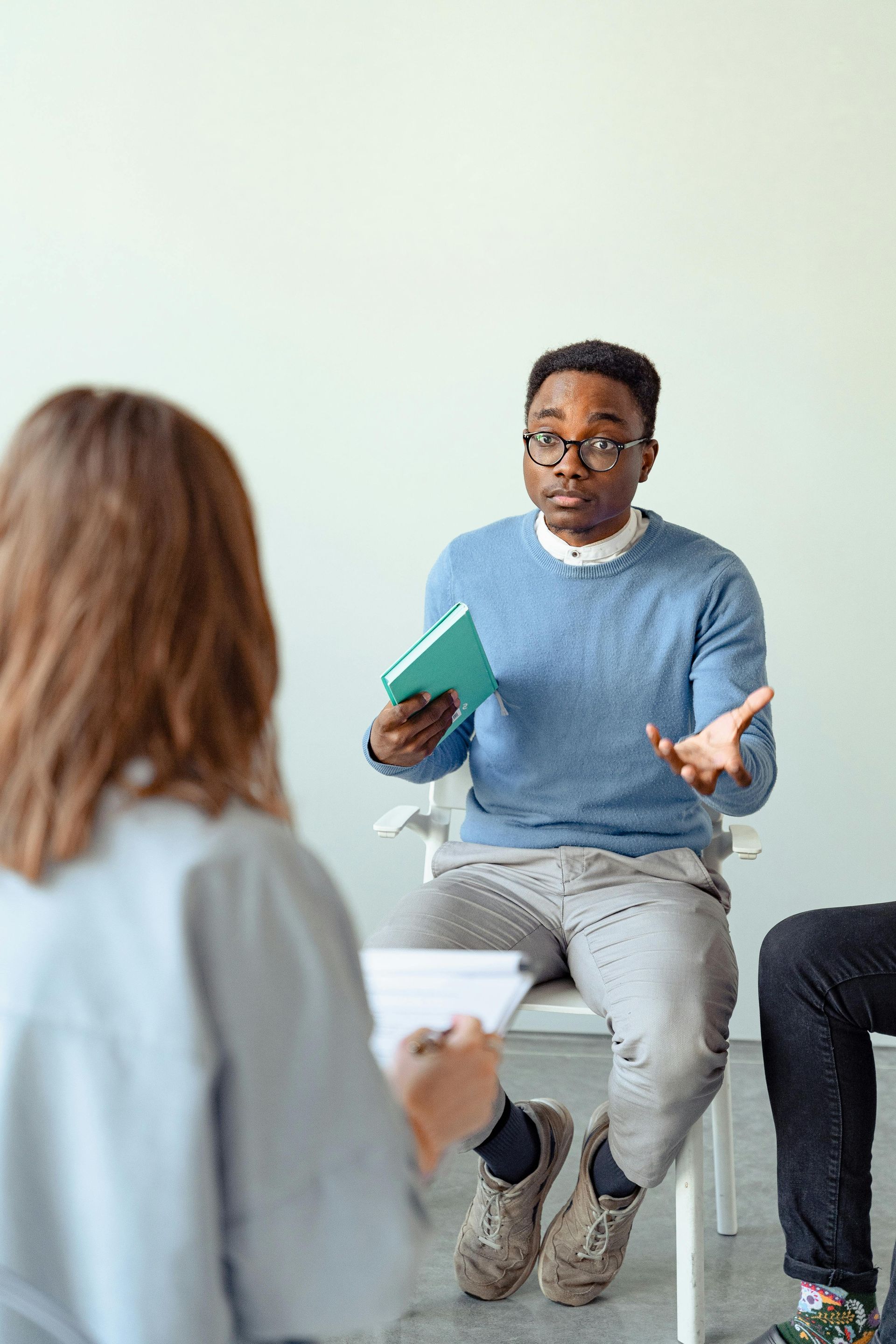 Man holding a notebook speaks during a seated discussion group in a bright room
