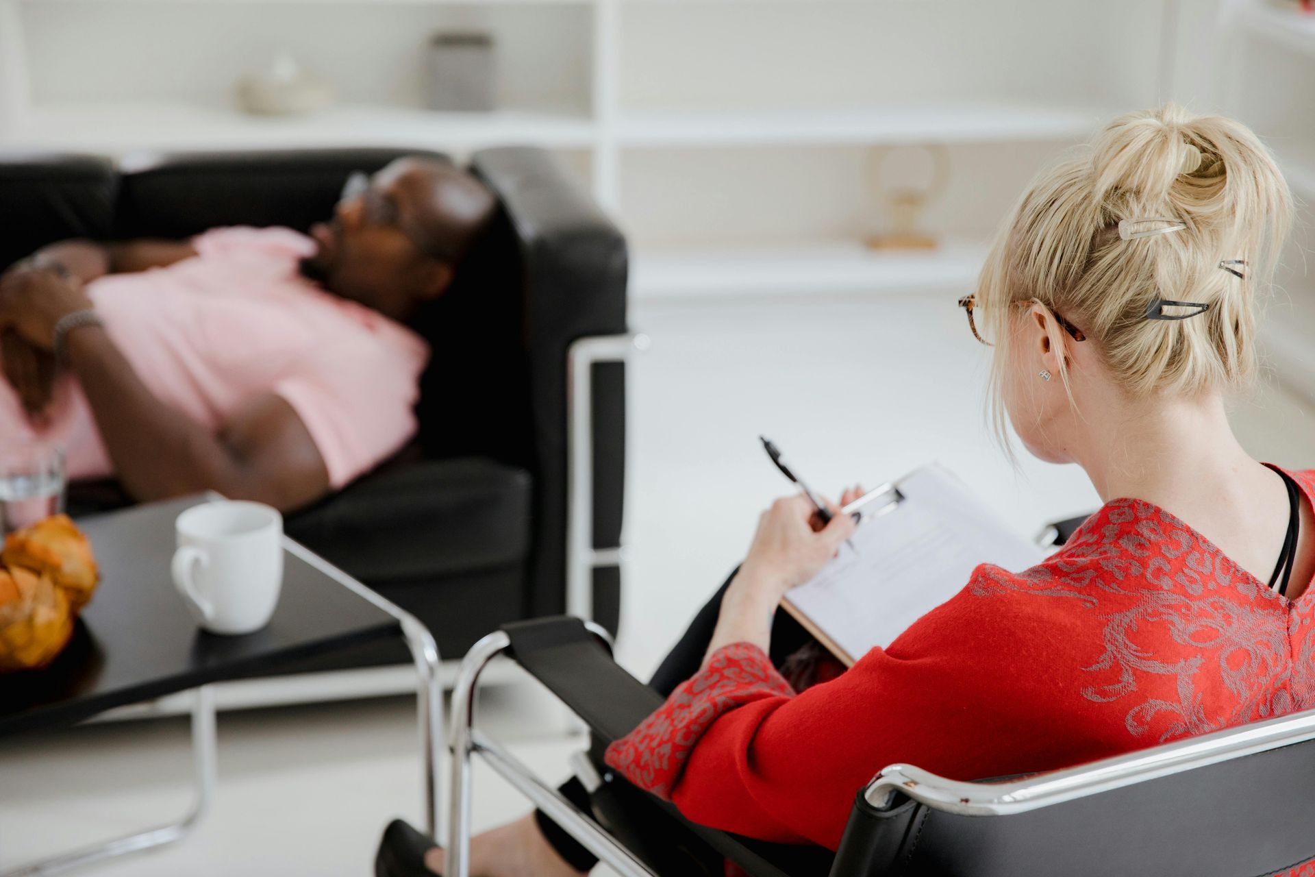 Therapist taking notes while a patient lies on a couch in a bright counseling office.