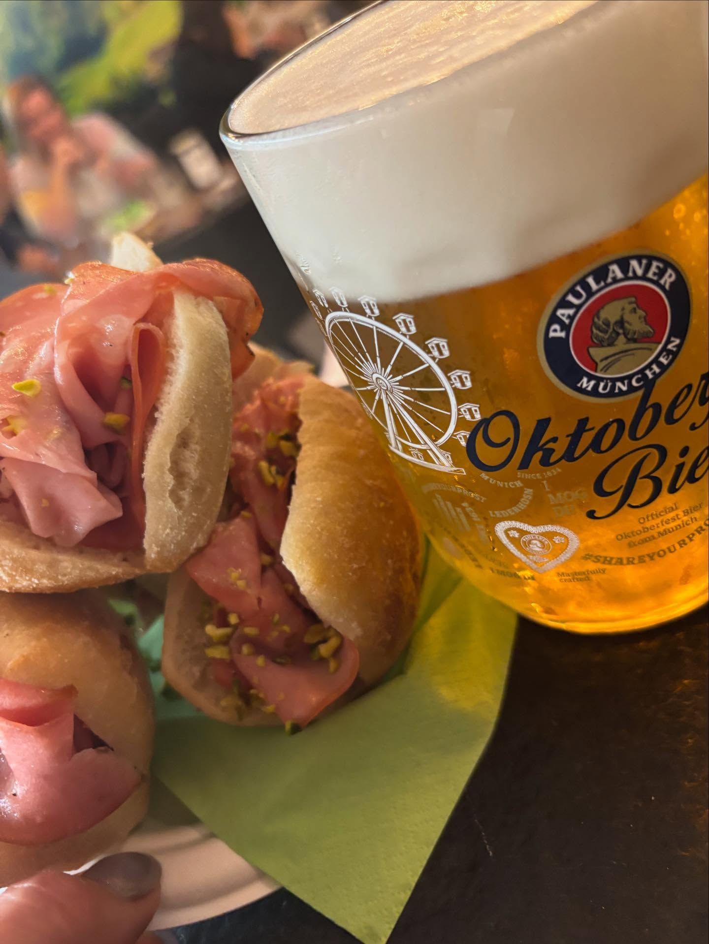 Boccale di birra accanto a un piatto di panini ripieni di carne su un tovagliolo verde a un tavolo dell'Oktoberfest.