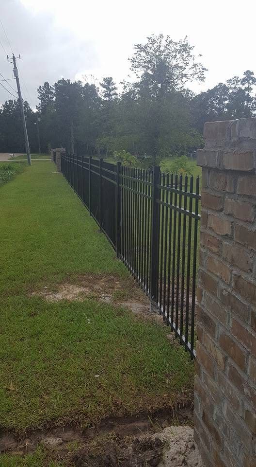 Black metal fence along grassy area, brick pillar on right.