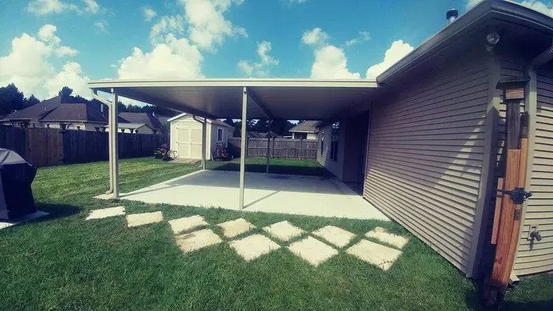 A patio with a covered roof, concrete slab, and stepping stones in a backyard, beside a house.