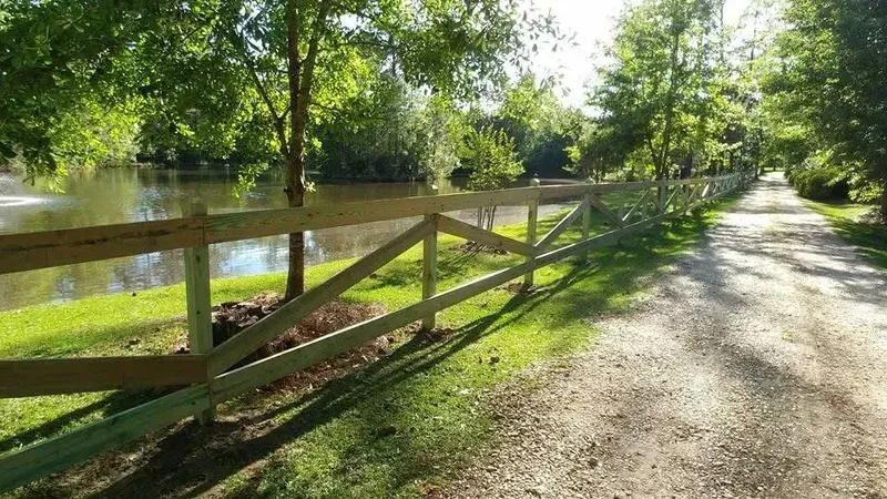 Wooden fence bordering a path alongside a lake with trees.