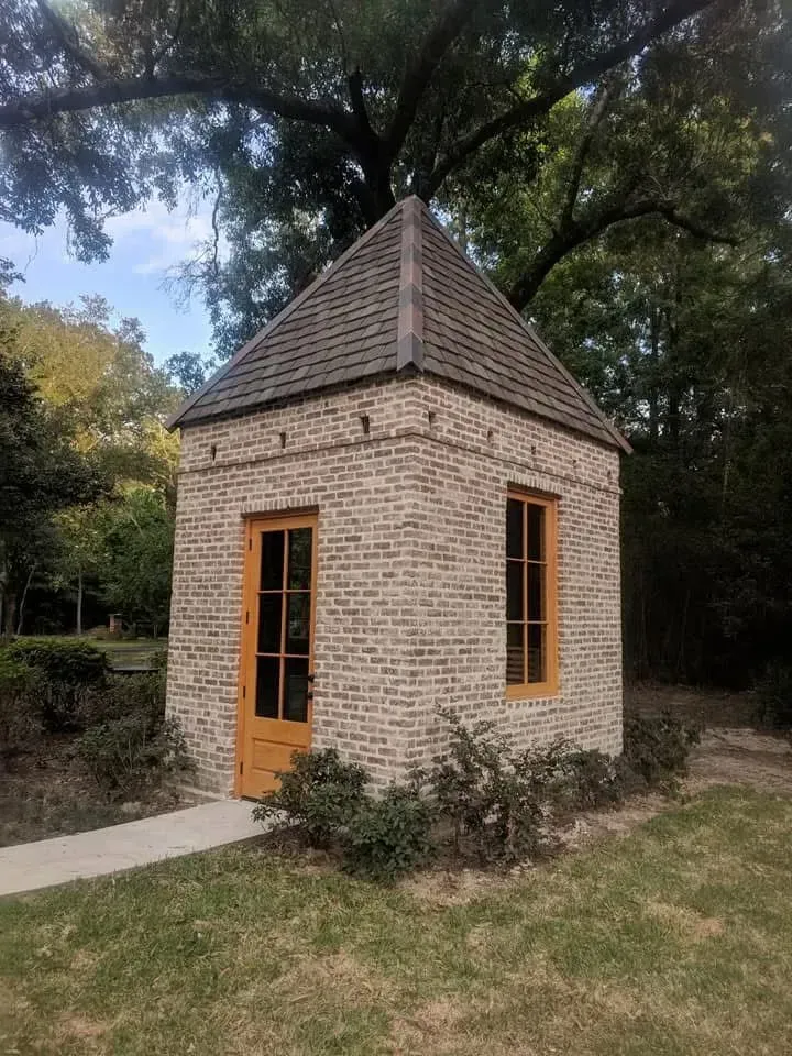 Small brick building with a pointed roof; orange door and window frames. Set in a grassy area.