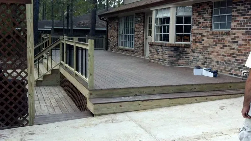 Wooden deck with stairs leading to a lower level, attached to a brick house. Lattice and railing.