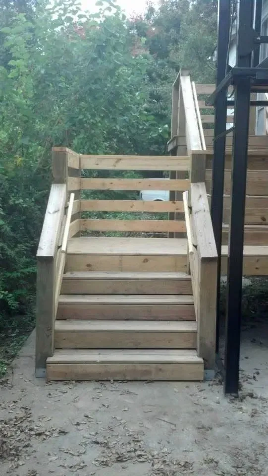 Wooden outdoor staircase with handrails, leading up to a platform.