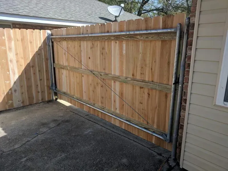 Wooden fence with metal-framed gate, closed. Gate has diagonal wire support. Outside a tan house on concrete.
