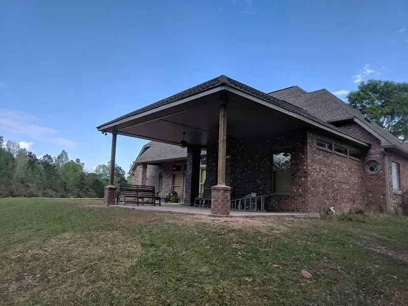 Brick house with a covered patio, set on a grassy lawn under a blue sky.