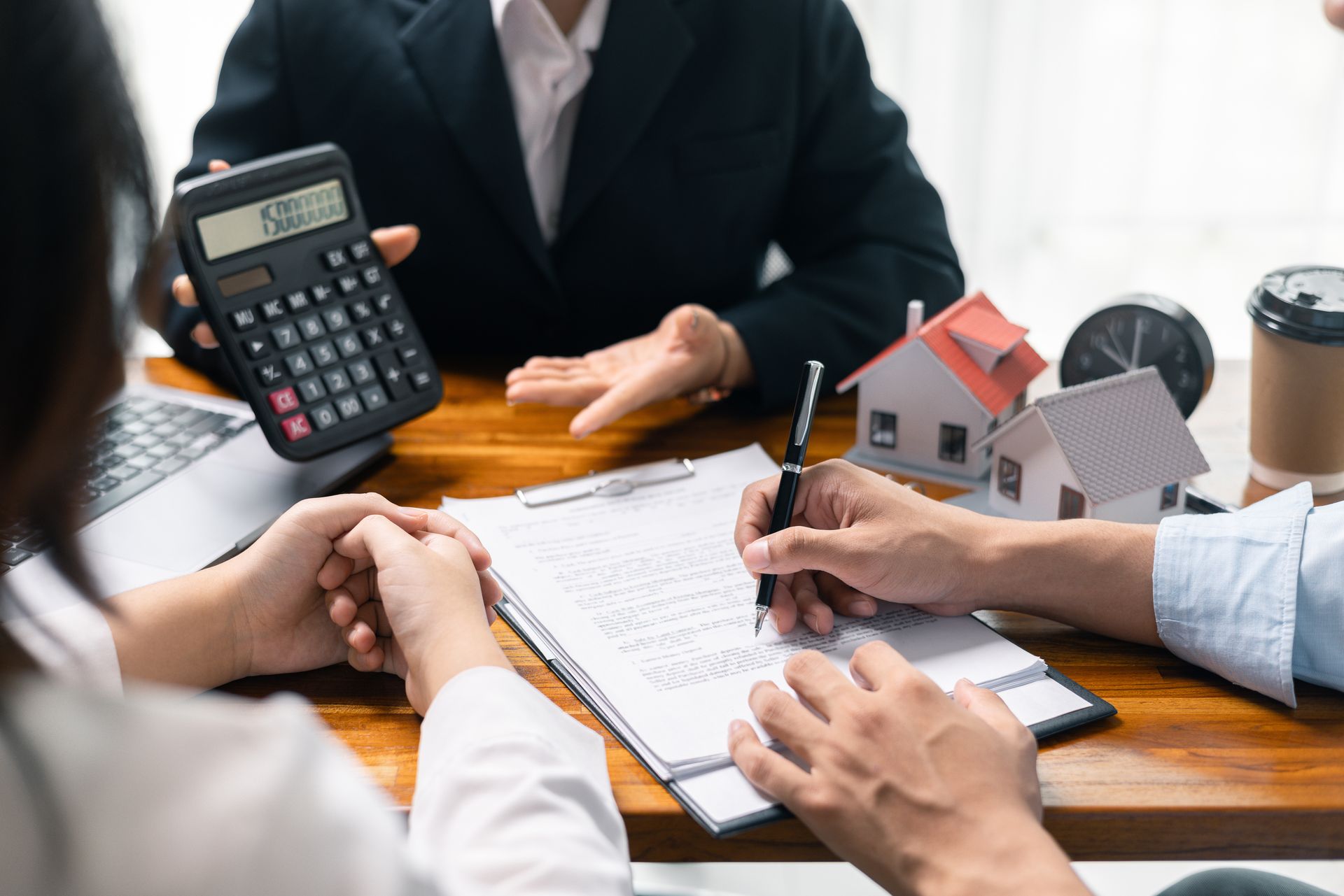 A group of people are sitting at a table with a calculator and a model house.