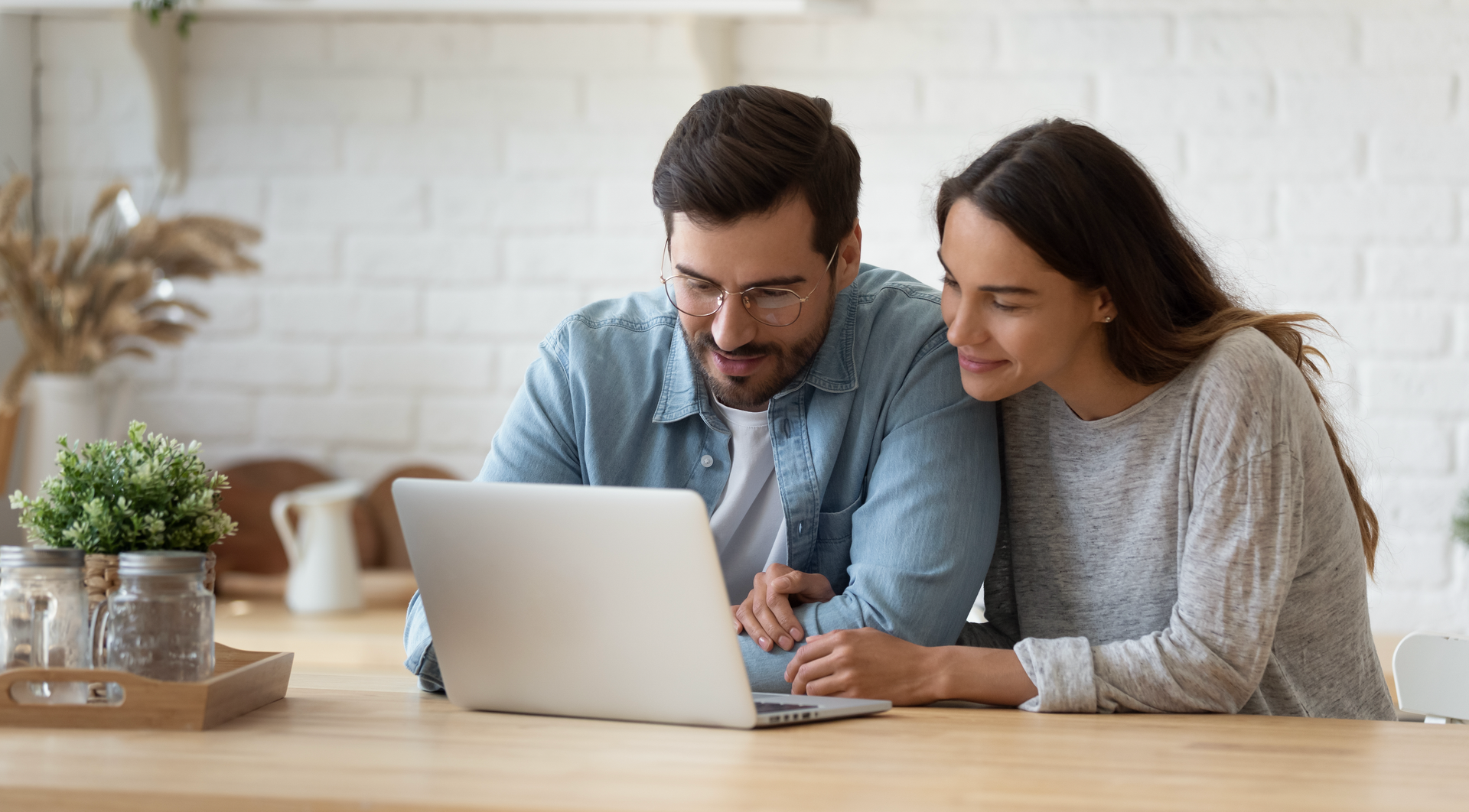 A man and a woman are sitting at a table looking at a laptop computer.