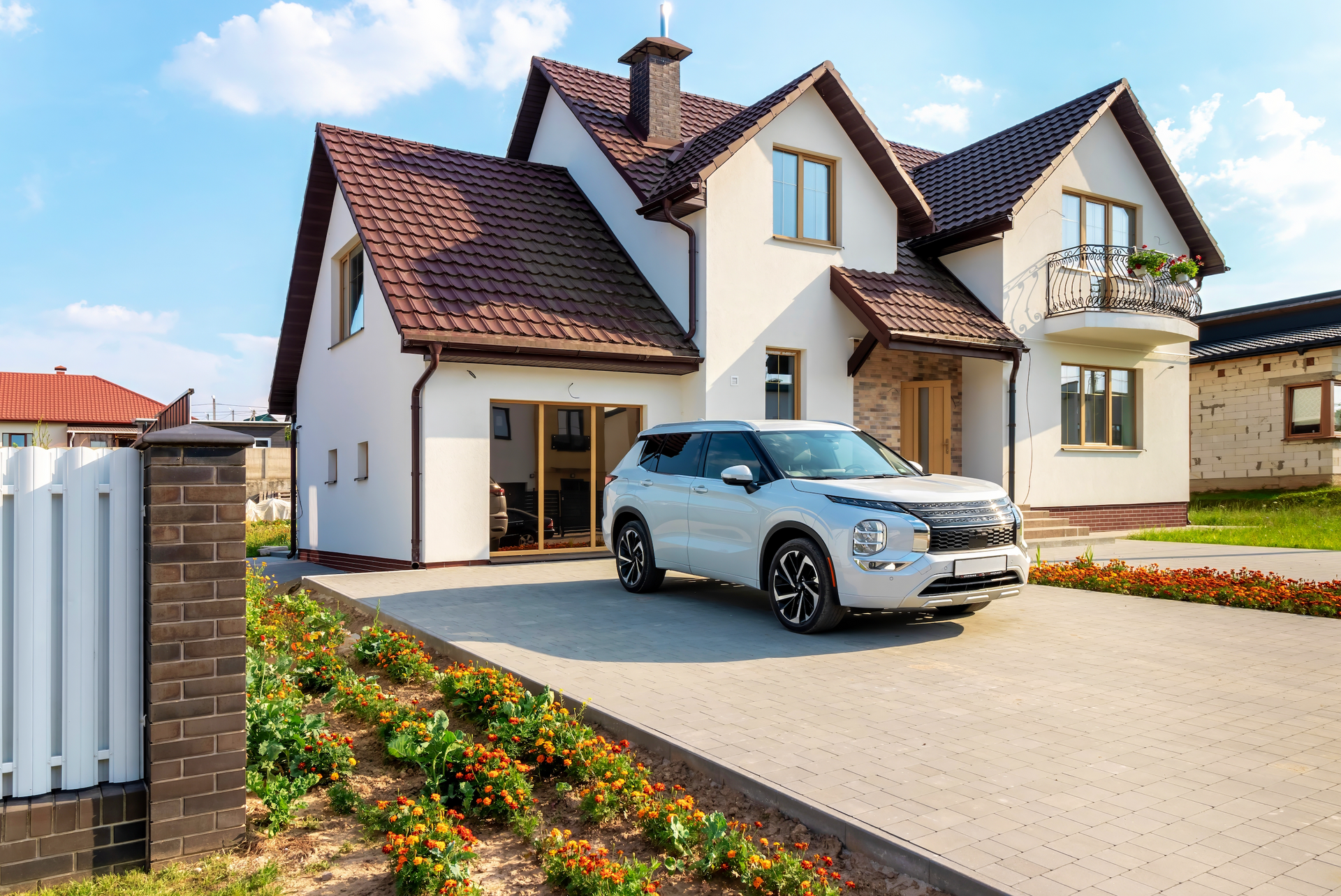 A white car is parked in front of a large white house.