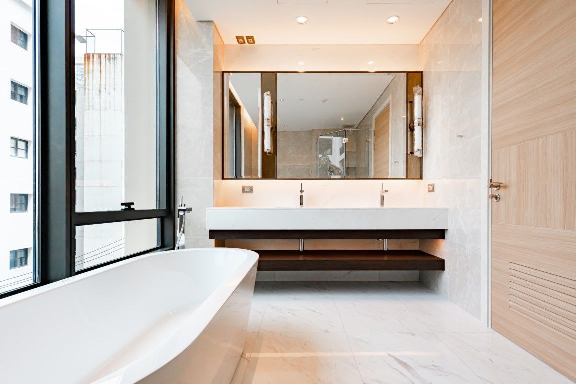 Modern bathroom with freestanding tub, large mirror, wood vanity, and bright natural light
