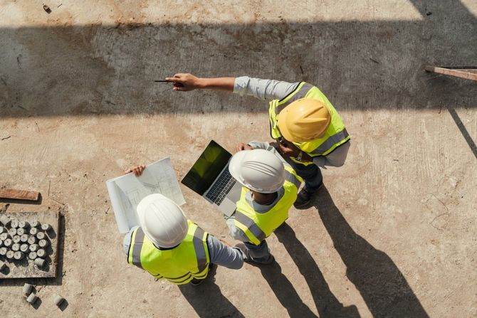 Two construction workers in hard hats and safety vests reviewing plans at a building site