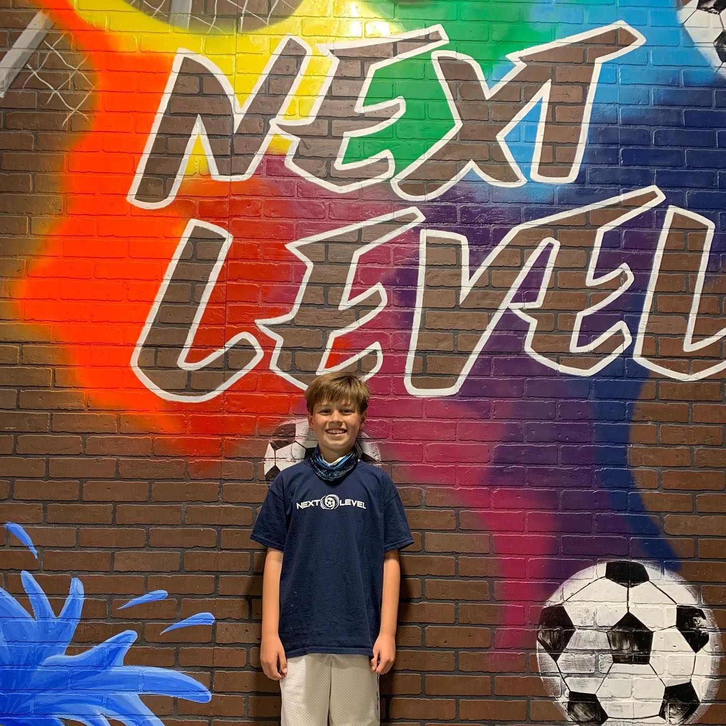 A boy is standing in front of a mural that says next level