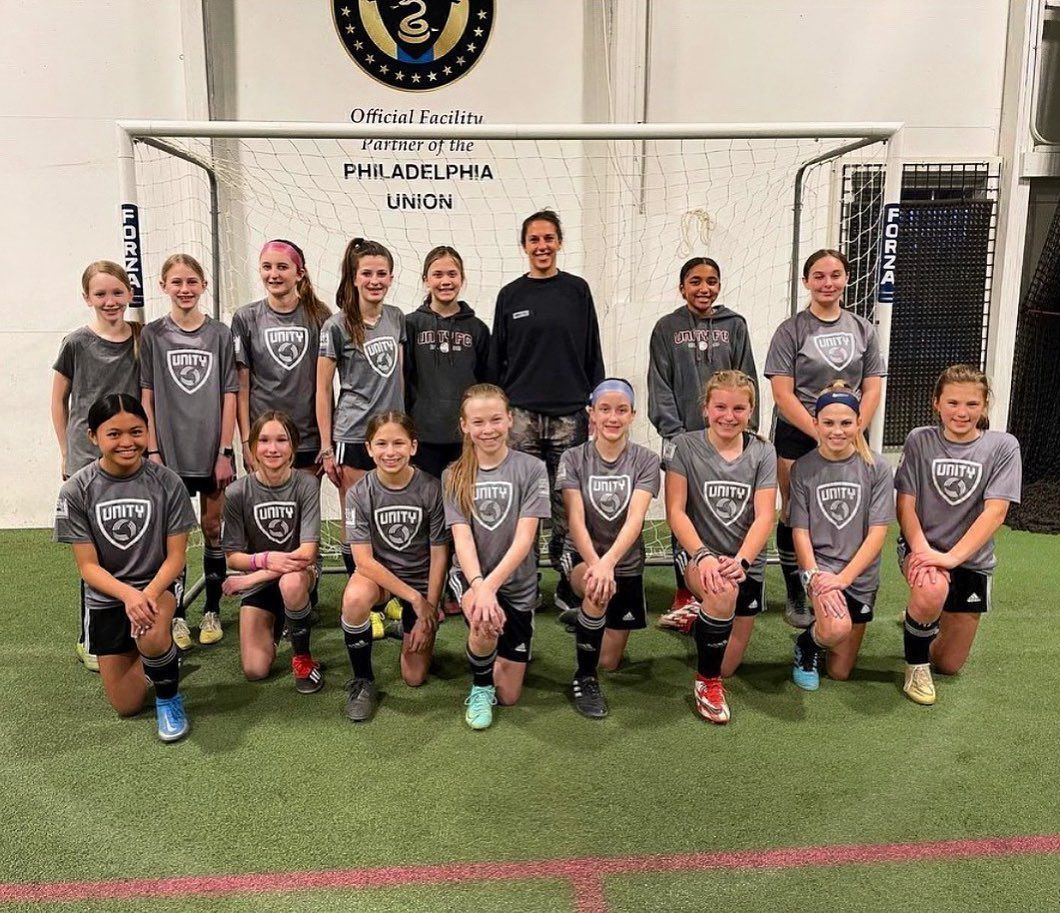 A group of young girls are posing for a picture on a soccer field.