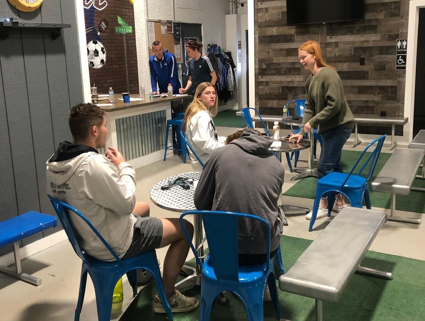 A group of people are sitting around tables and benches in a room.