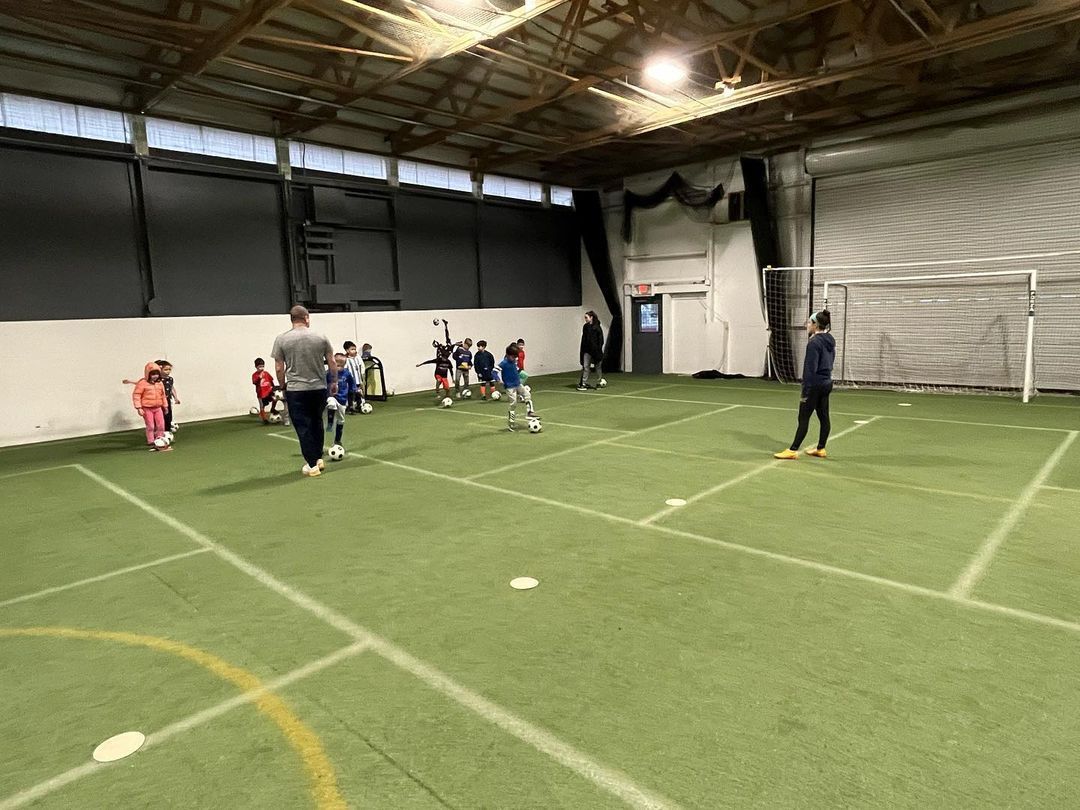 A group of children are playing soccer in an indoor stadium.