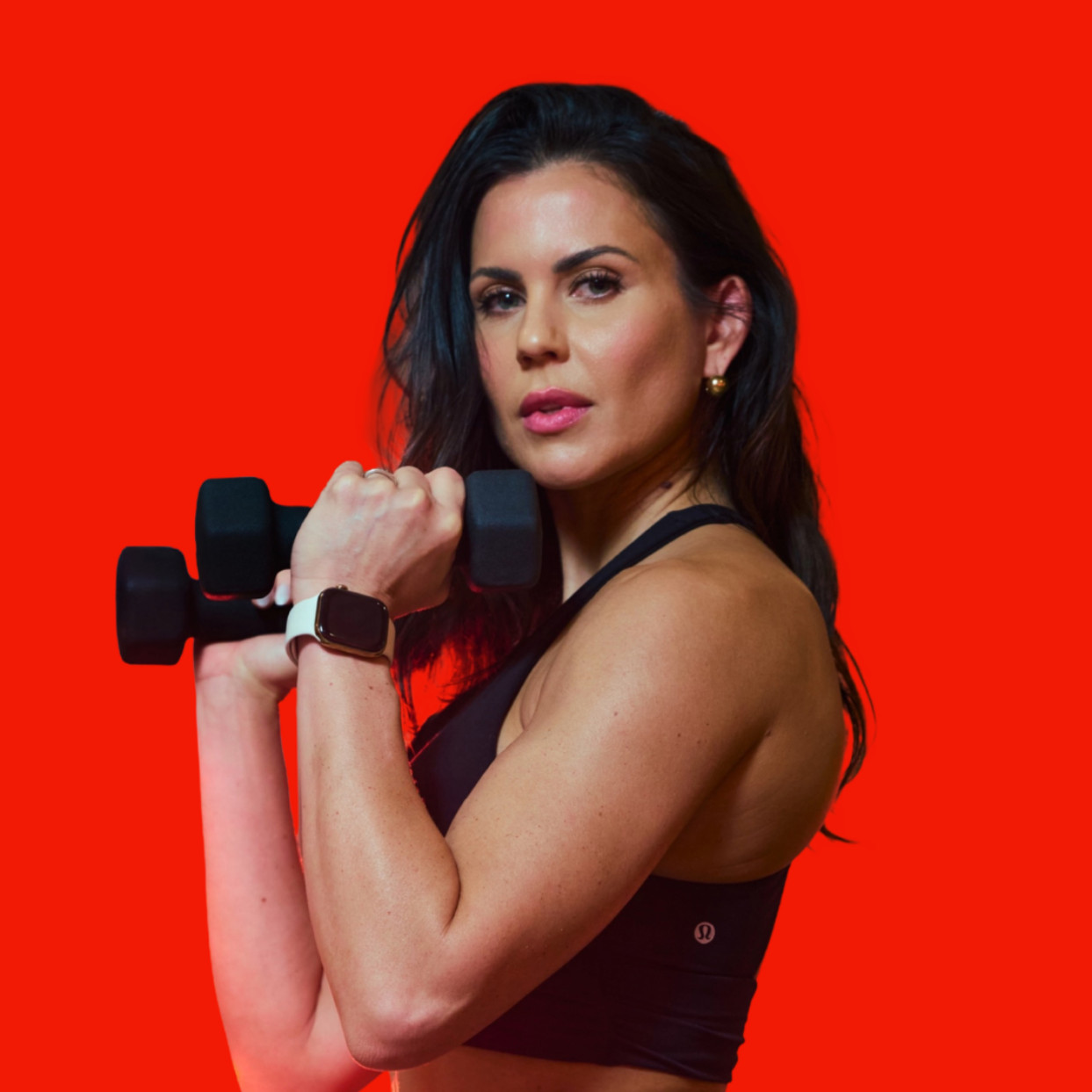 Closeup of a woman with long dark hair holding weights with a bright red background.