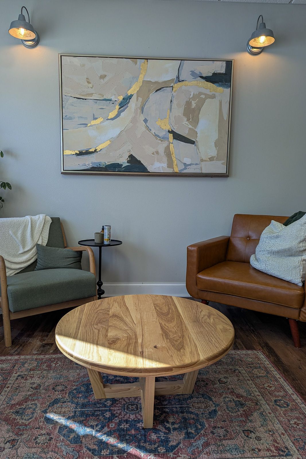 Round white ash coffee table with splayed legs on a patterned rug between armchairs. Story City, Iowa.