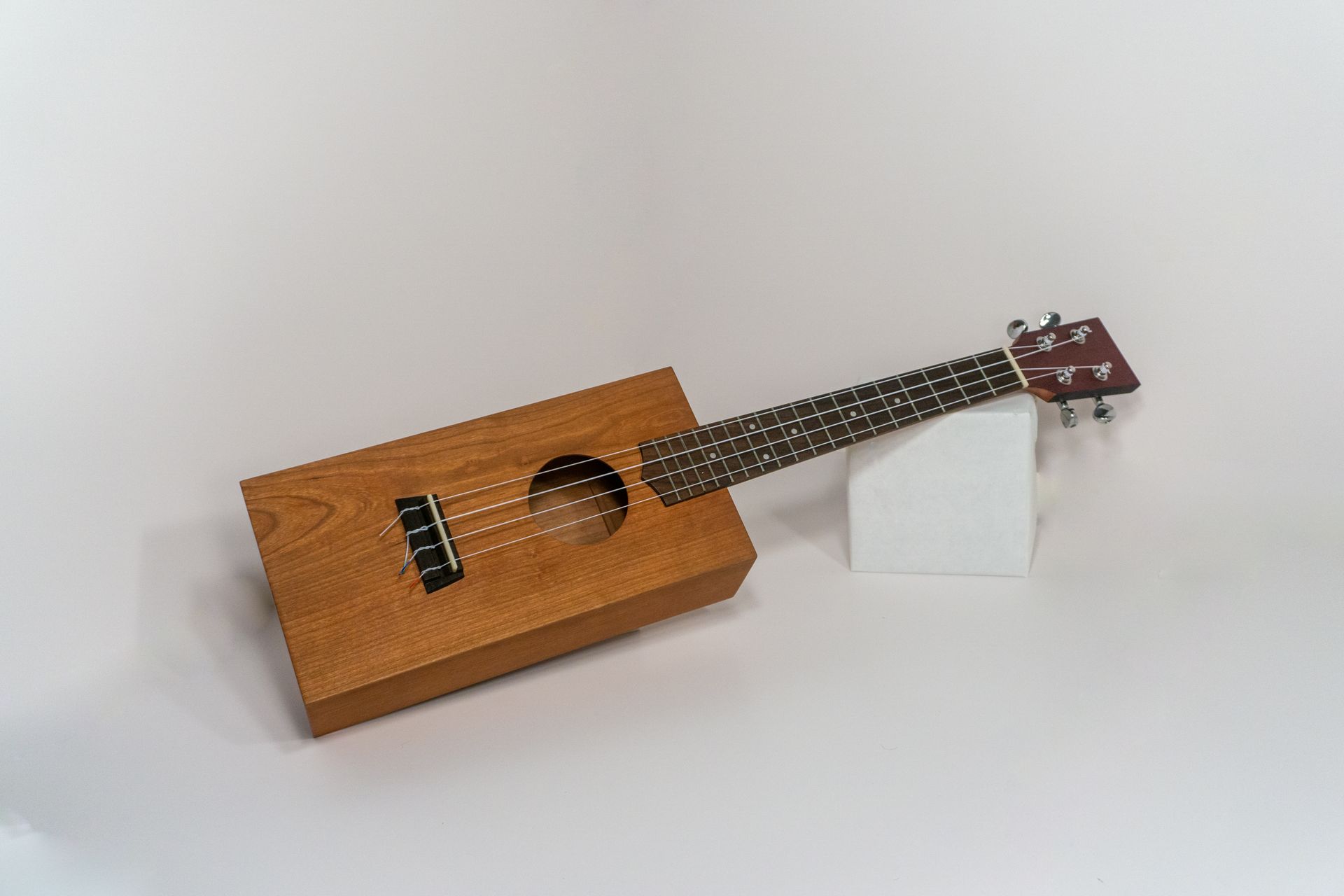 Handcrafted wooden ukulele with a rectangular body made from cherry wood, showcasing custom luthiery  by Crow and Timber.