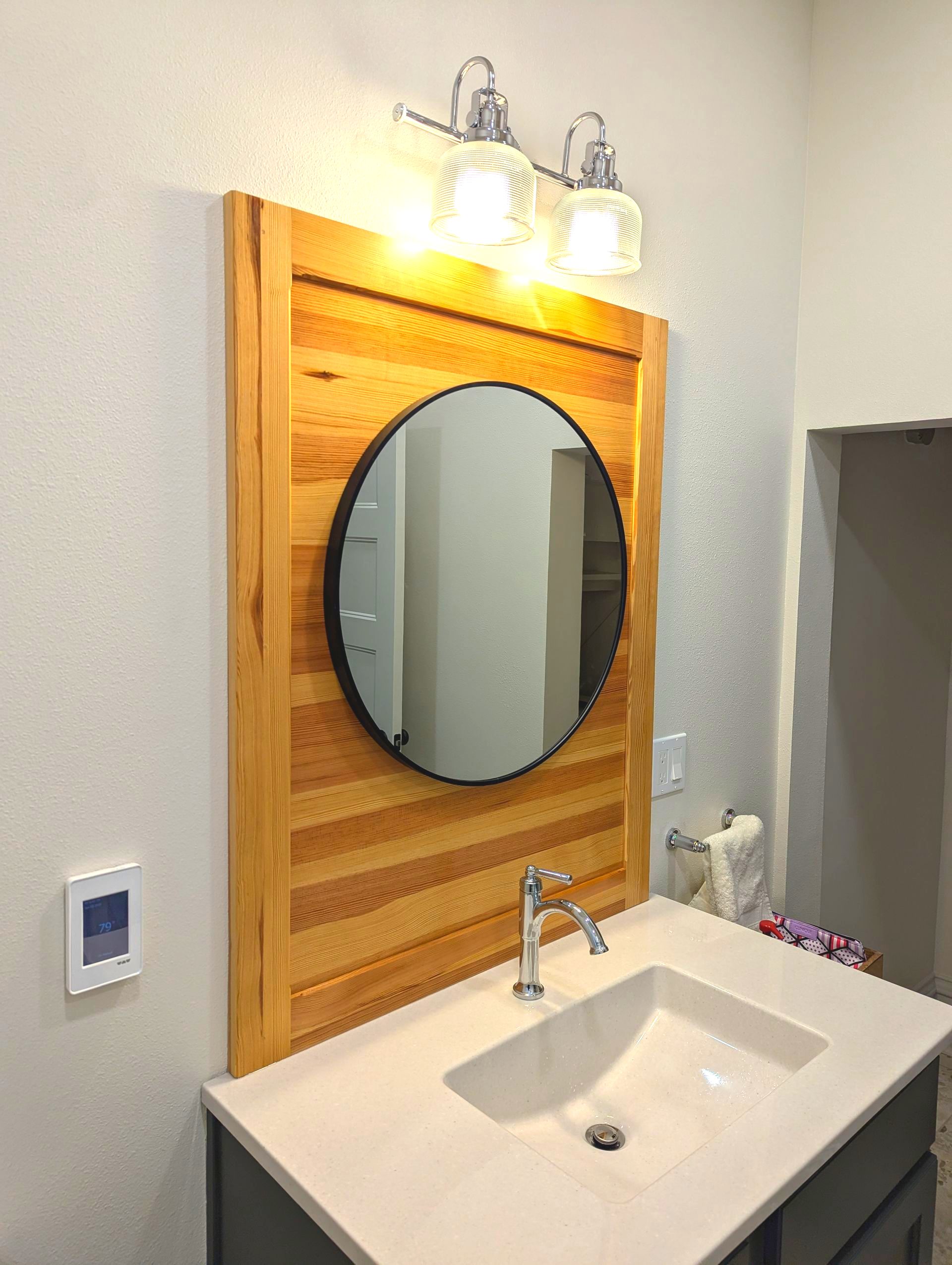 Round mirror with black edge framed in reclaimed wood flooring, handcrafted by Crow and Timber.