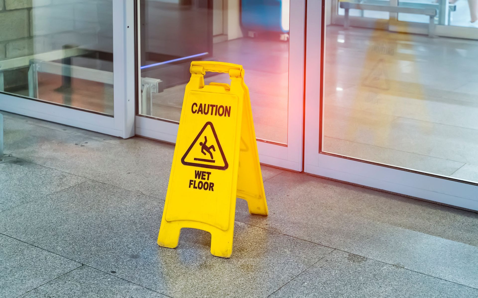 Yellow wet floor caution sign on a polished indoor floor near glass doors.